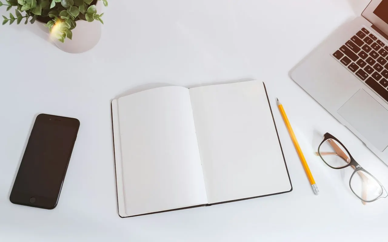 Ordinateur portable, téléphone et carnet ouverts sur une table blanche