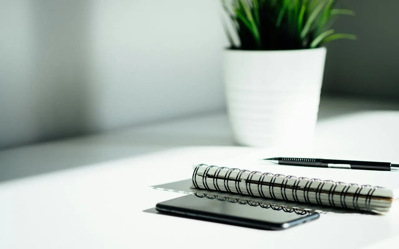 Carnet à spirale et téléphone devant une plante en pot
